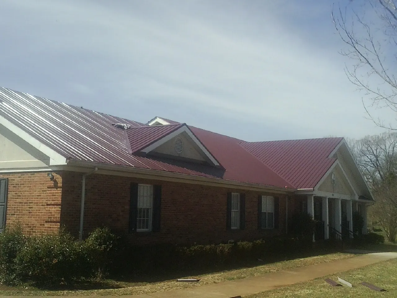 Red metal roof with gabled entries on a long brick building, from a Hail Damage Roof Repair job in Schuyler