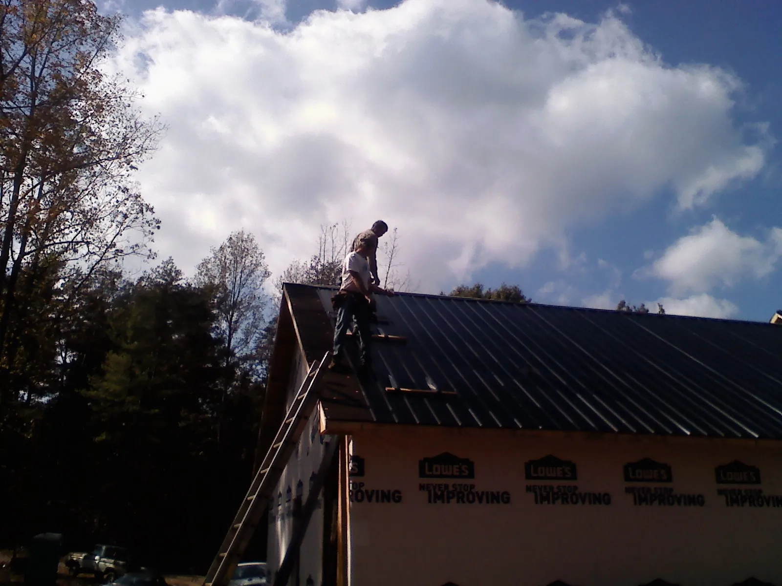 Roofer fastening dark metal panels high against a cloudy sky, from a Roof Inspection job in Schuyler